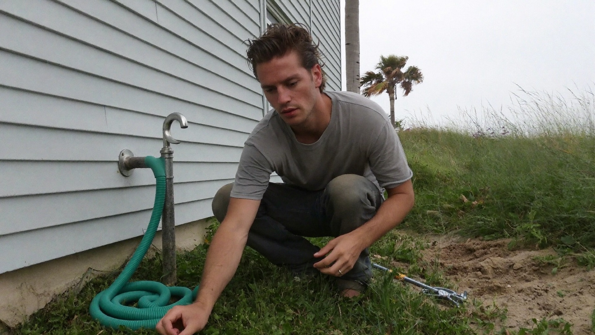 A plumber working on an outdoor shower riser at the side of a coastal Florida house